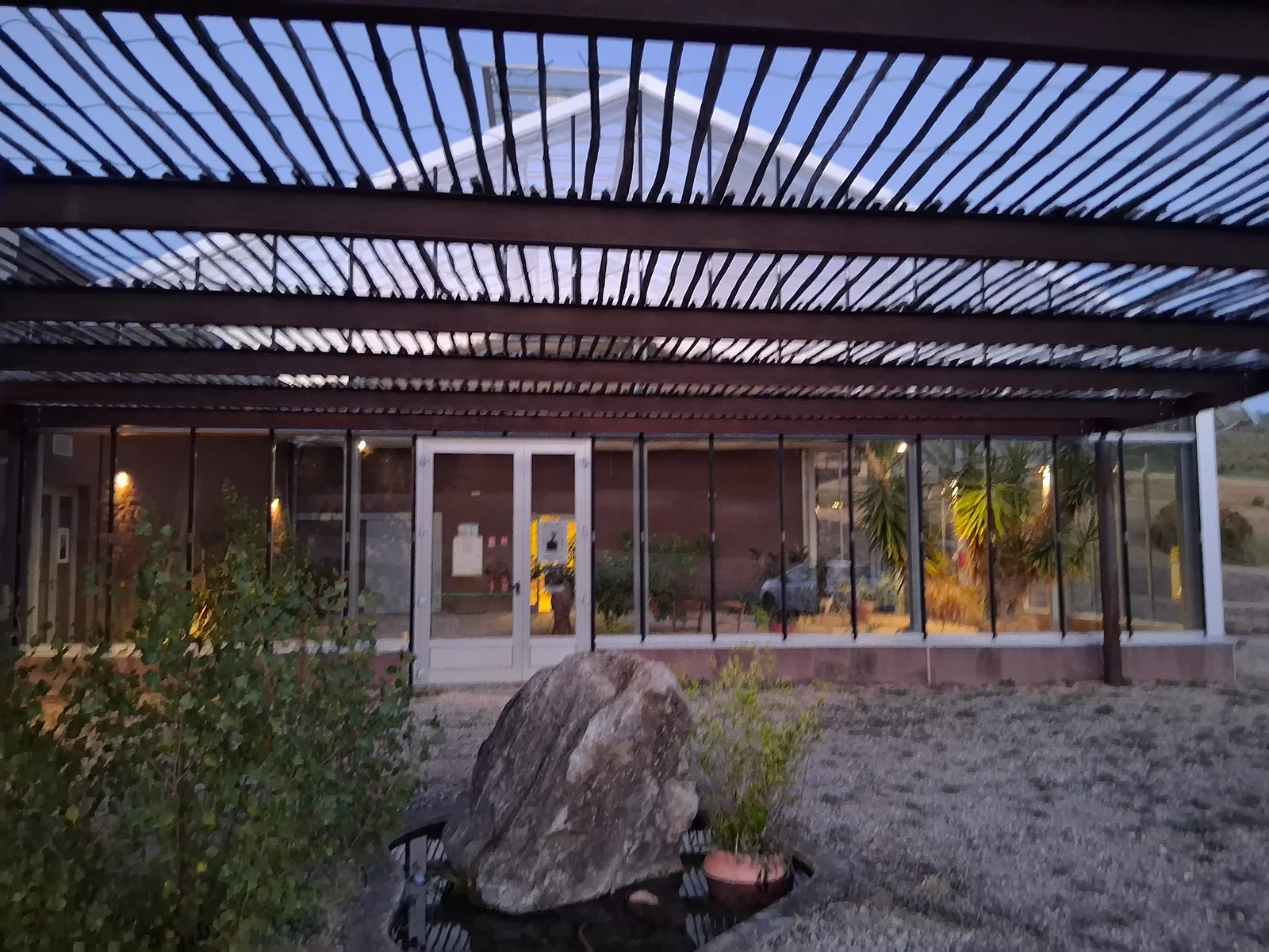 La pergola du centre culturel au crépuscule, éclairée par la lumière chaleureuse des pièces voisines.